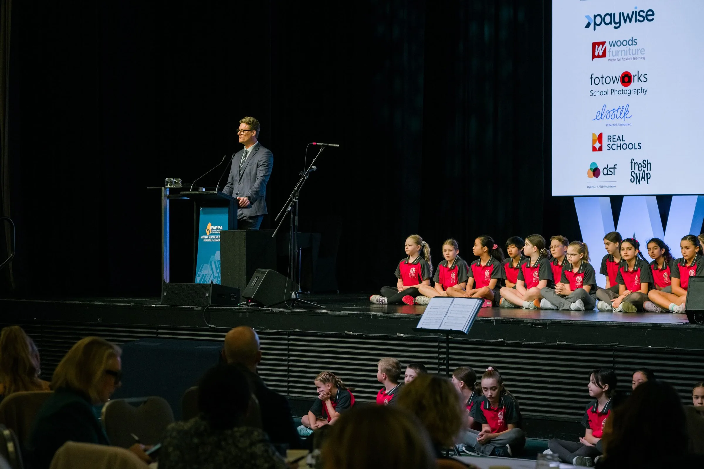 Event MC speaking on stage in front of a seated group